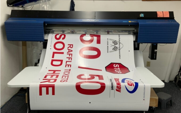 A red and white banner advertising 50/50 raffle tickets for sale at a company fundraising event printing out of a state-of-the-art Roland digital printer.